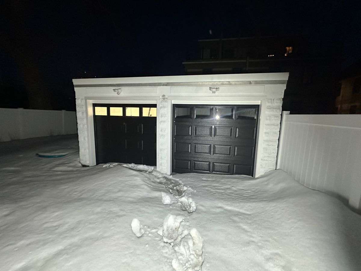 Two black garage doors with windows on white garage in snowy winter — Massachusetts