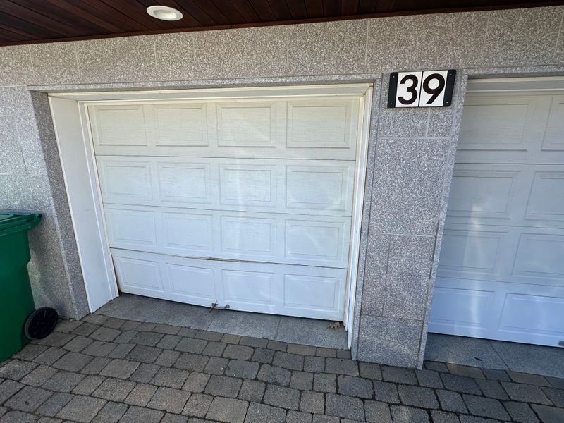 Damaged white raised-panel garage door misaligned in frame before repair — Massachusetts